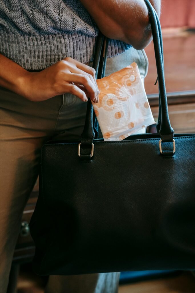 Crop faceless female in casual clothes putting panty liner in package in black leather handbag